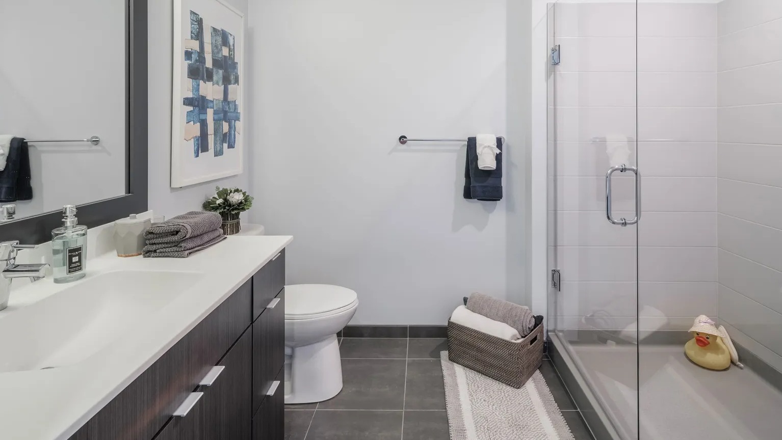 Modern bathroom with dark vanity, wide mirror, and glass-enclosed walk-in shower at 1000 South Clark apartments in Chicago
