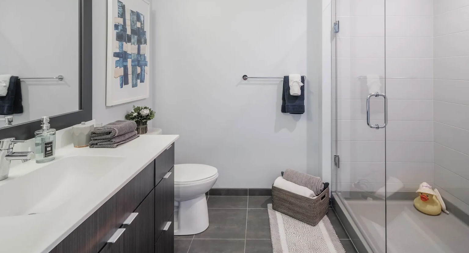 Modern bathroom with dark vanity, wide mirror, and glass-enclosed walk-in shower at 1000 South Clark apartments in Chicago