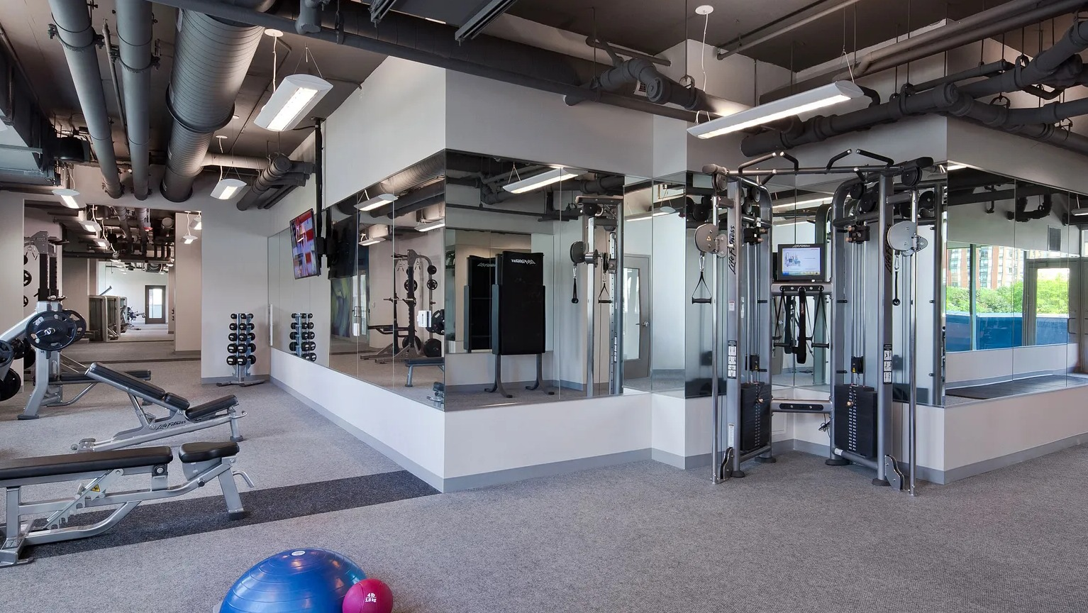 Spacious fitness center with strength machines, mirrored walls, and large windows at 1000 South Clark apartments in Chicago