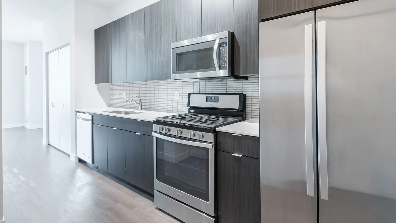 Modern galley kitchen with sleek dark cabinetry, tile backsplash, and stainless steel Whirlpool appliances at 1000 South Clark apartments