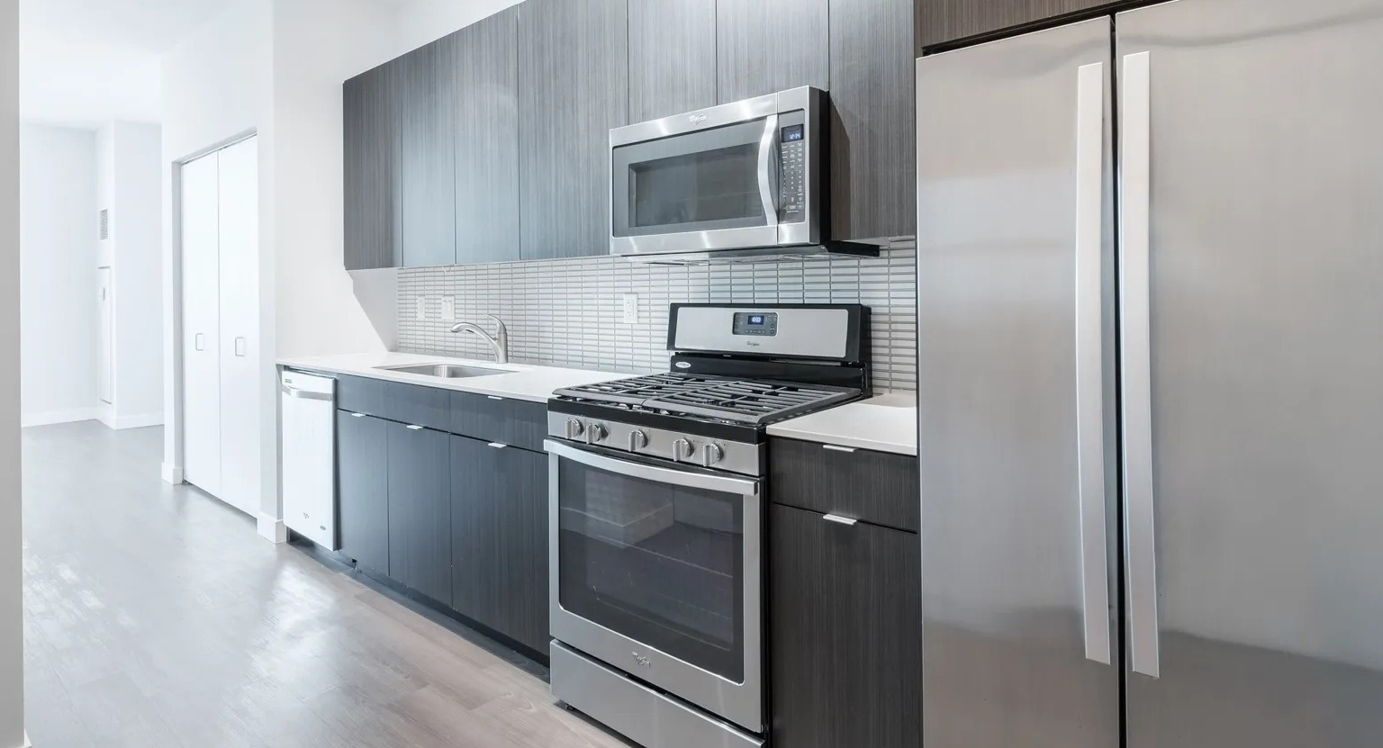 Modern galley kitchen with sleek dark cabinetry, tile backsplash, and stainless steel Whirlpool appliances at 1000 South Clark apartments