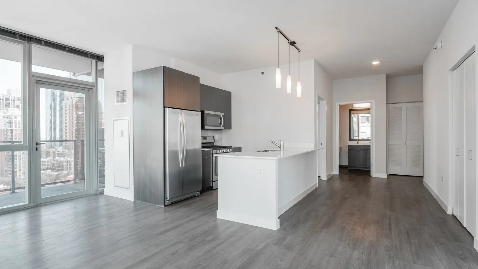 Modern open-concept living space with floor-to-ceiling windows, sleek kitchen, and pendant lighting at 1000 South Clark apartments in Chicago