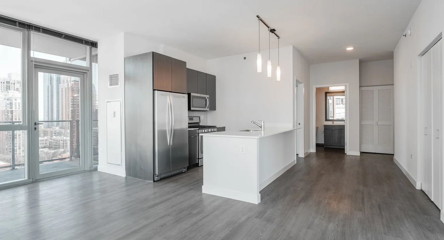 Modern open-concept living space with floor-to-ceiling windows, sleek kitchen, and pendant lighting at 1000 South Clark apartments in Chicago