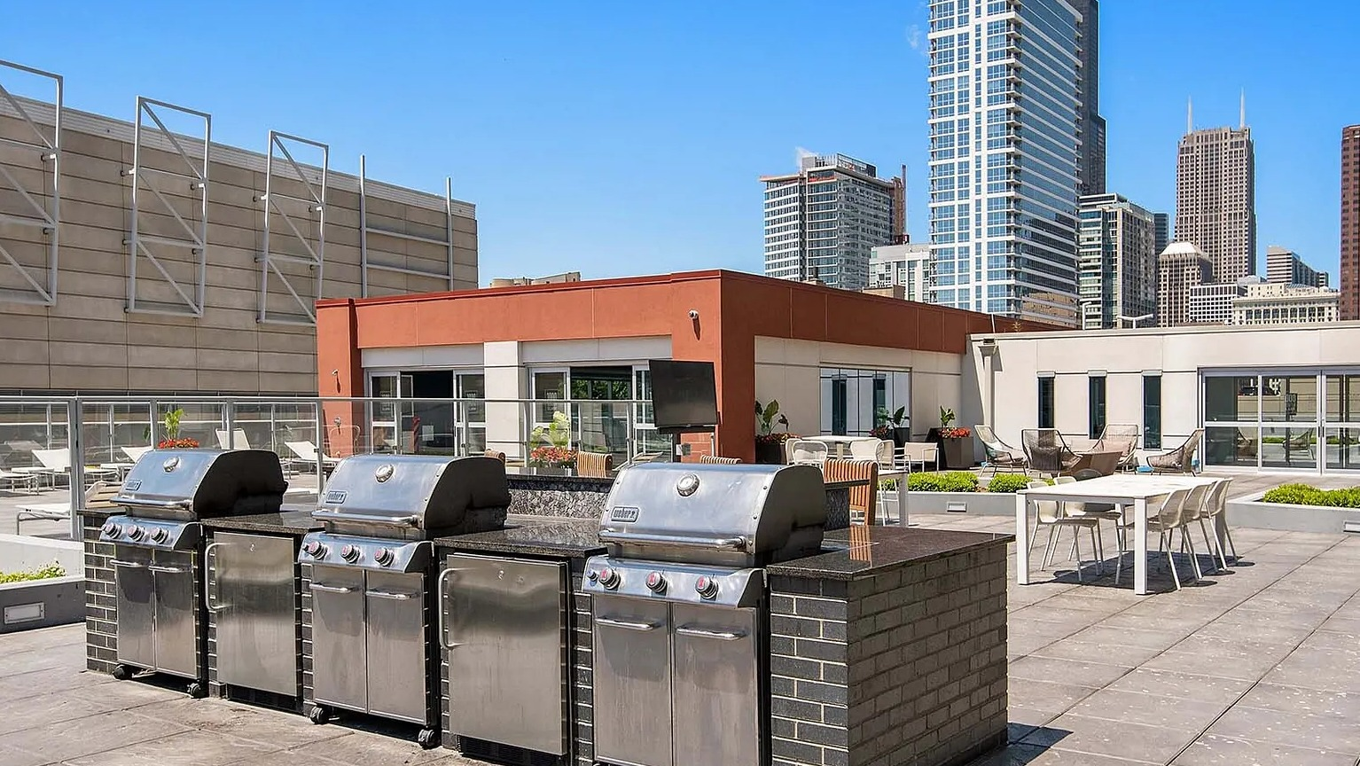 Rooftop grilling stations with stainless steel barbecues and city skyline backdrop at 1000 South Clark apartments in Chicago