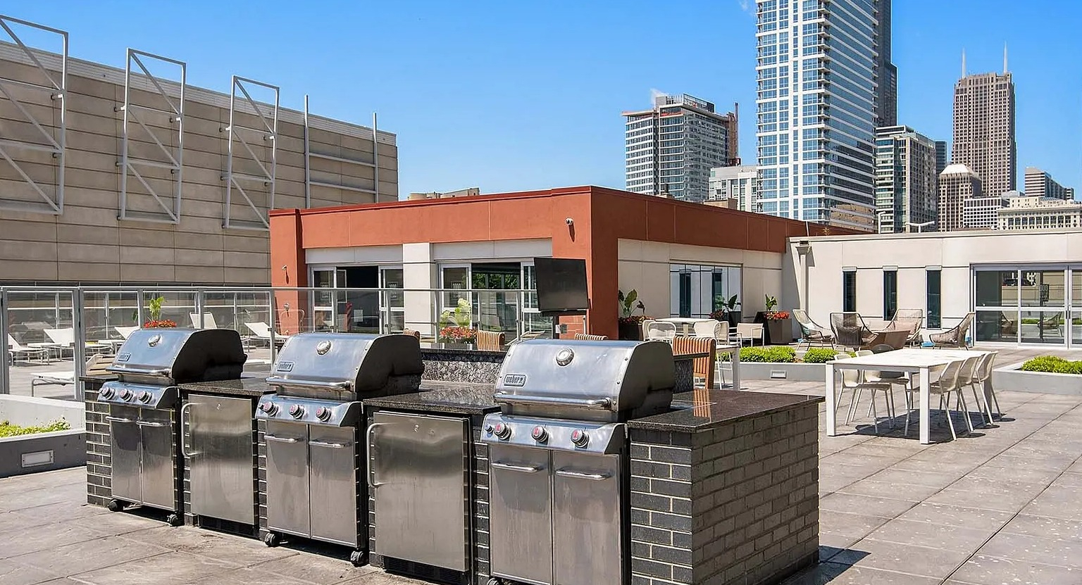 Rooftop grilling stations with stainless steel barbecues and city skyline backdrop at 1000 South Clark apartments in Chicago