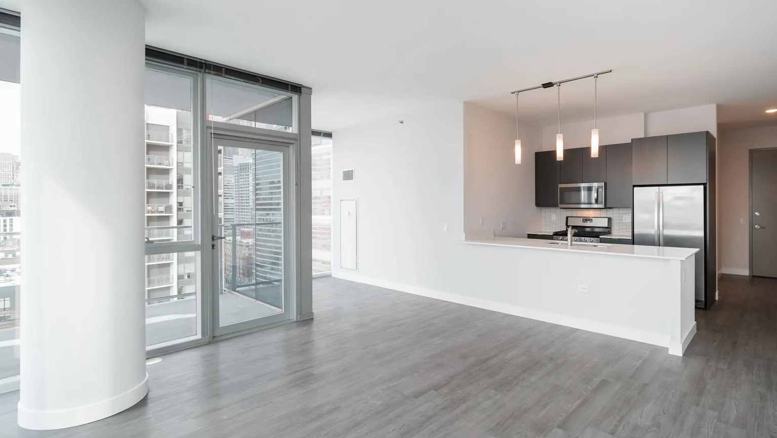 Bright spacious living room with pillar detail, modern kitchen, and balcony access at 1000 South Clark apartments in Chicago