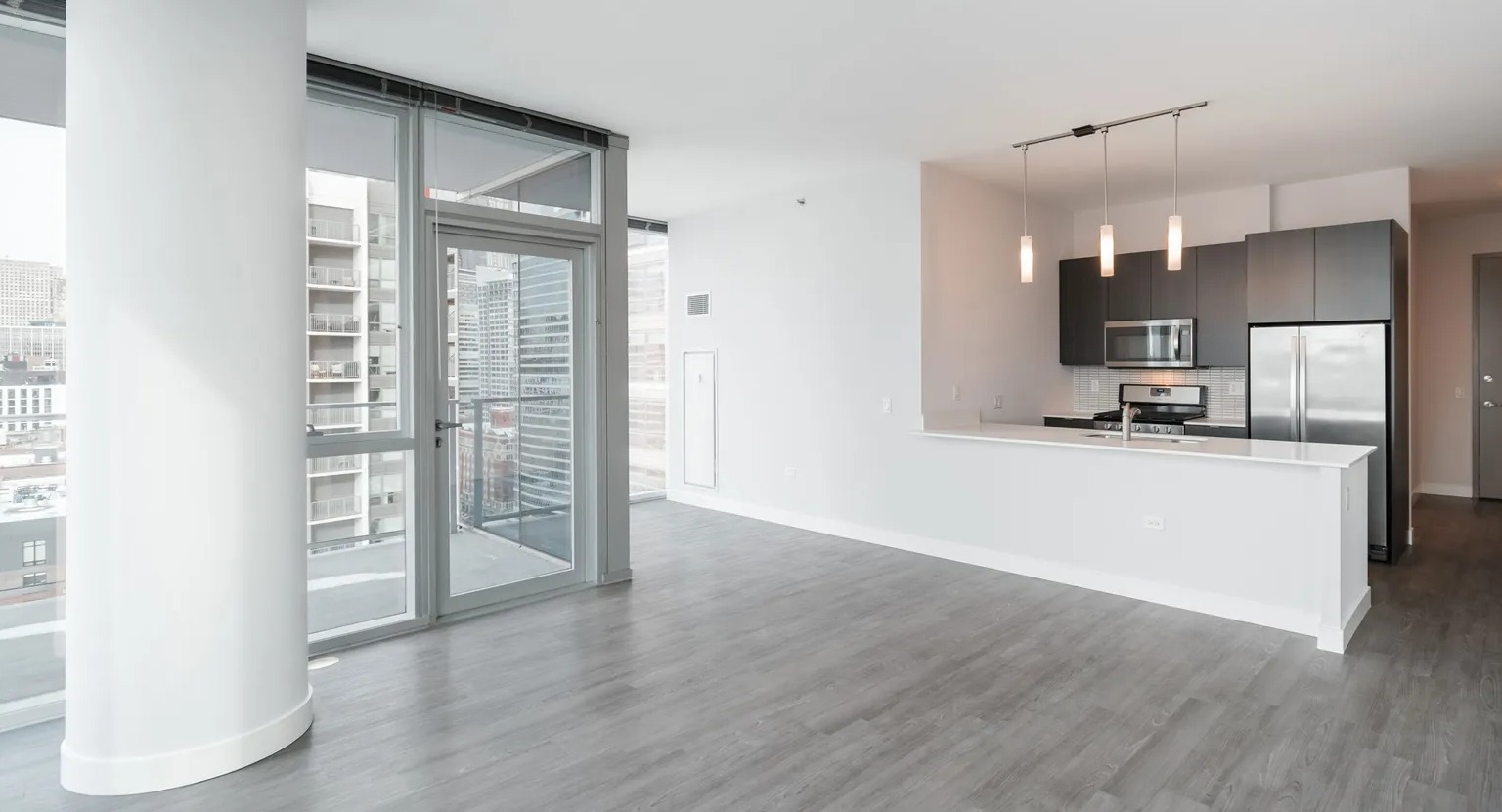 Bright spacious living room with pillar detail, modern kitchen, and balcony access at 1000 South Clark apartments in Chicago