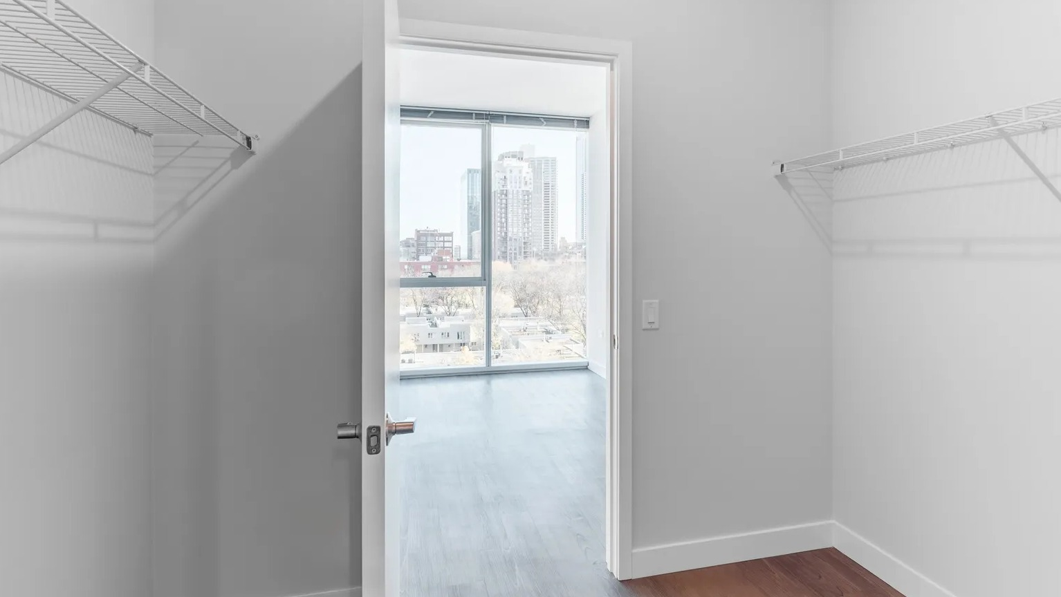 Spacious walk-in closet with dual wire shelving and a view into a bright bedroom with large windows at 1000 South Clark apartments in Chicago