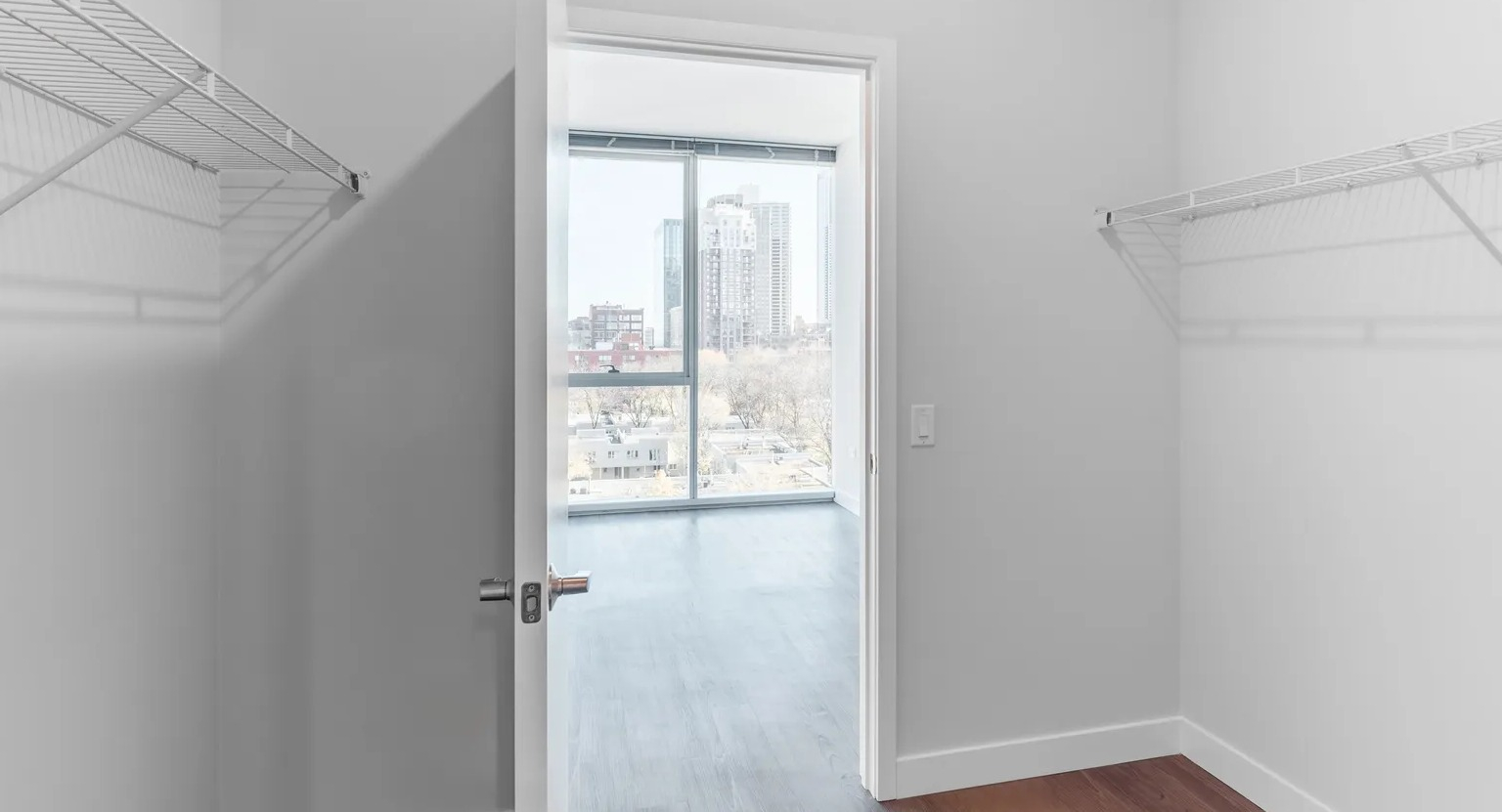 Spacious walk-in closet with dual wire shelving and a view into a bright bedroom with large windows at 1000 South Clark apartments in Chicago