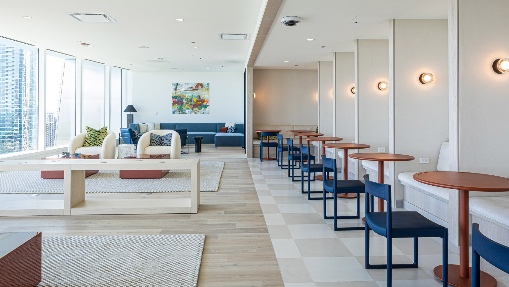 Bright coworking lounge with individual tables, booth seating, and floor-to-ceiling windows overlooking Chicago at 1000M Apartments