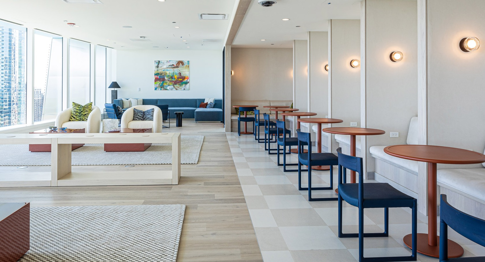 Bright coworking lounge with individual tables, booth seating, and floor-to-ceiling windows overlooking Chicago at 1000M Apartments