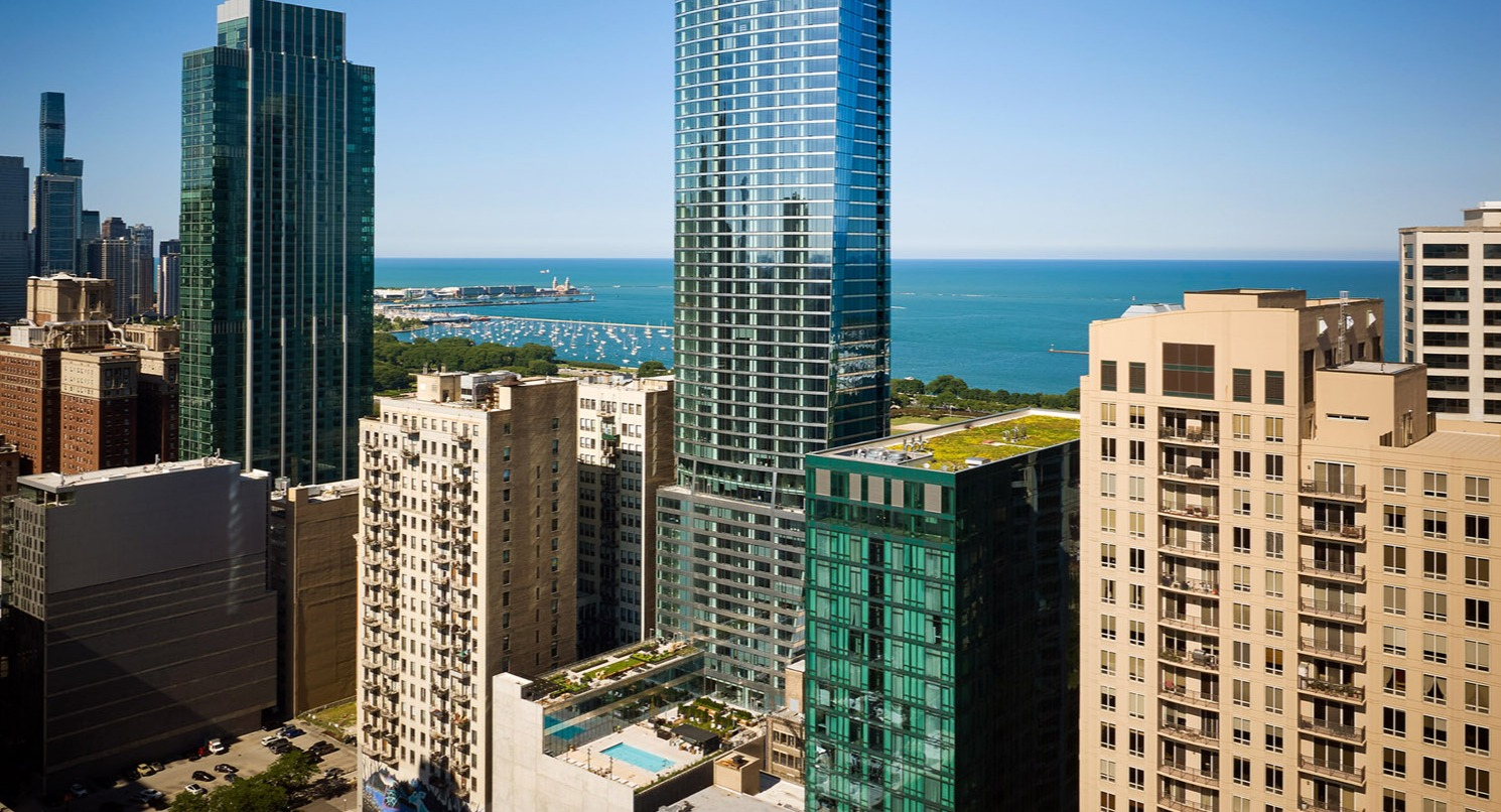 Tall glass residential tower of 1000M Apartments rising above downtown Chicago with views of Lake Michigan in the background