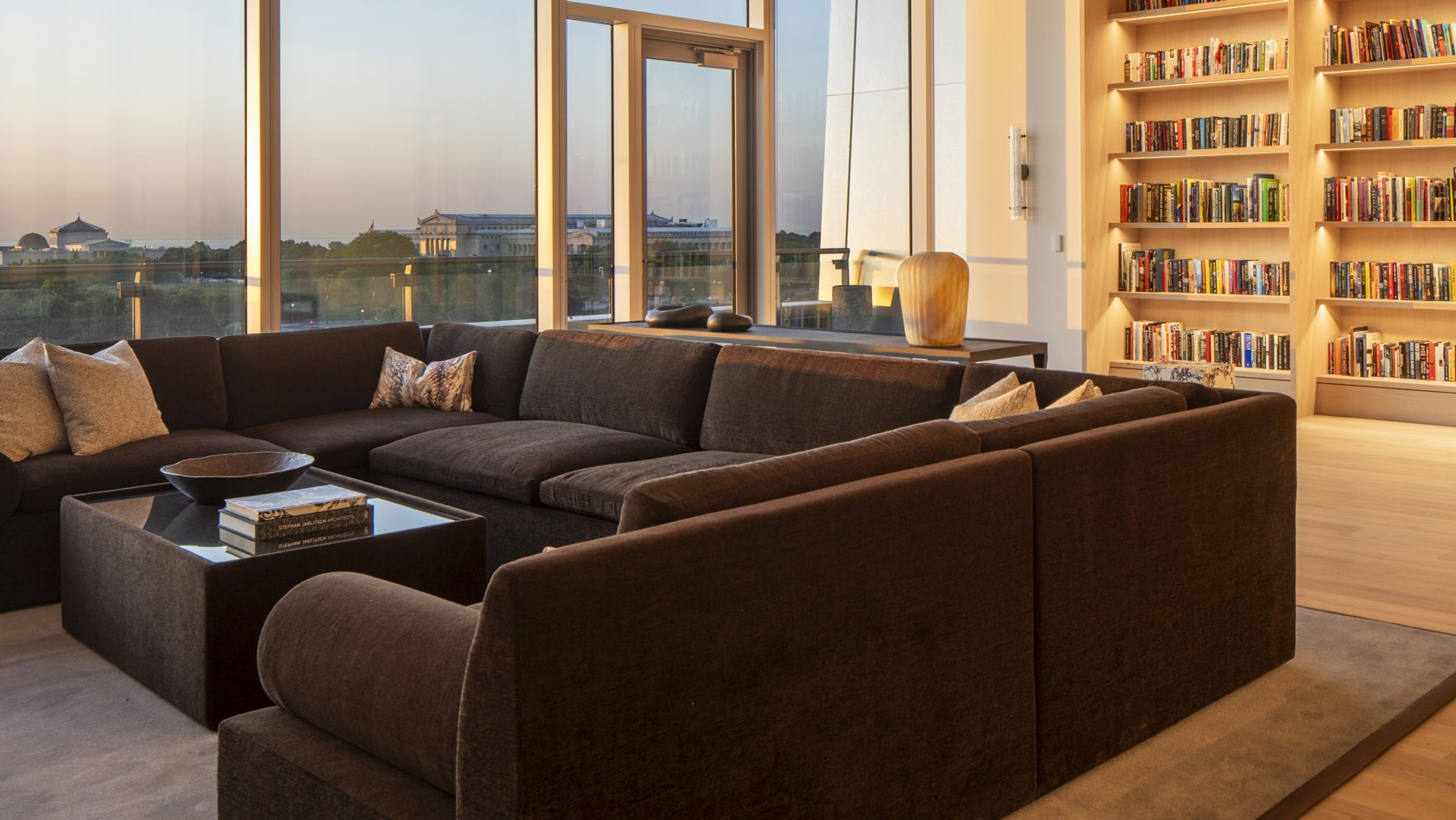 Cozy library lounge with wall-to-wall bookshelves, large sectional seating, and warm sunset views toward Grant Park at 1000M Apartments in Chicago