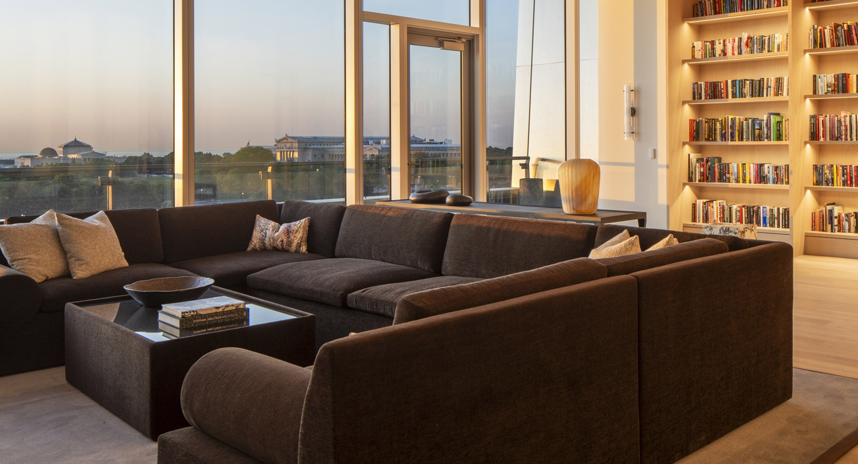 Cozy library lounge with wall-to-wall bookshelves, large sectional seating, and warm sunset views toward Grant Park at 1000M Apartments in Chicago