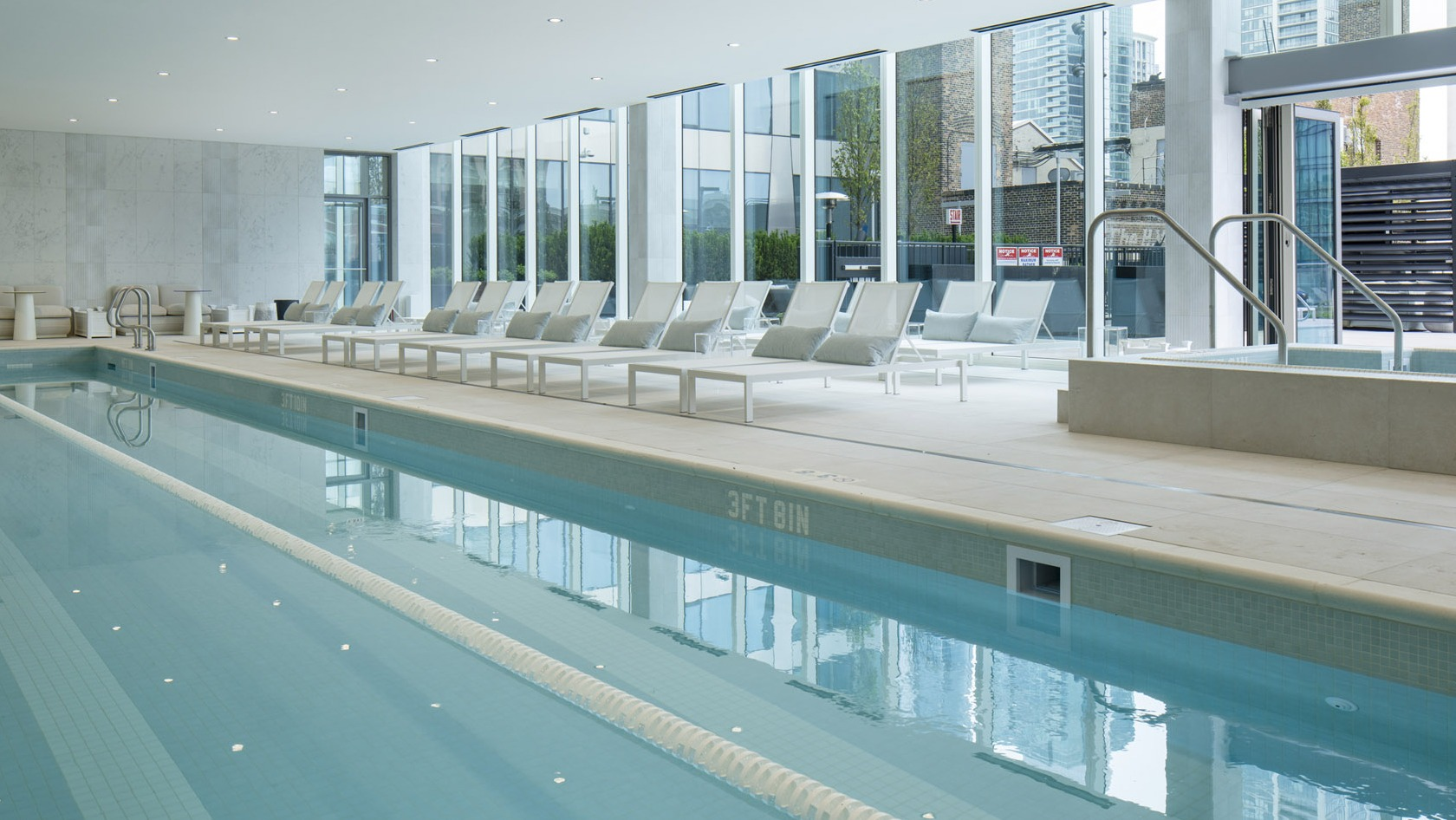 Spacious indoor swimming pool with lap lanes, modern lounge chairs, and floor-to-ceiling windows at 1000M Apartments in Chicago