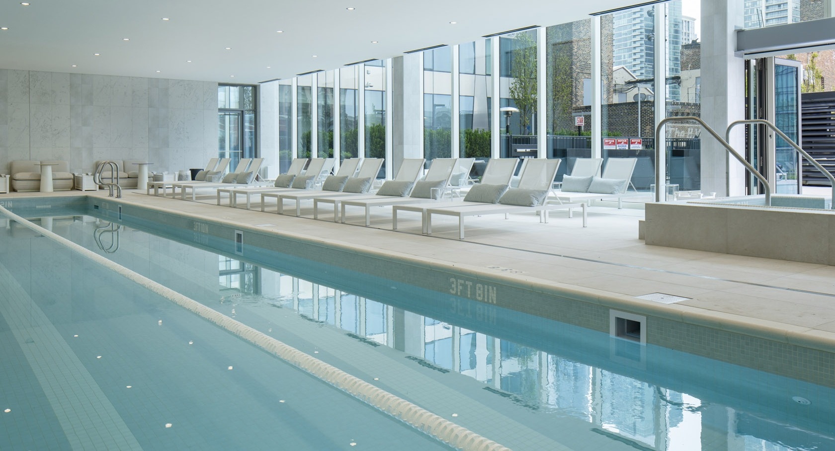 Spacious indoor swimming pool with lap lanes, modern lounge chairs, and floor-to-ceiling windows at 1000M Apartments in Chicago