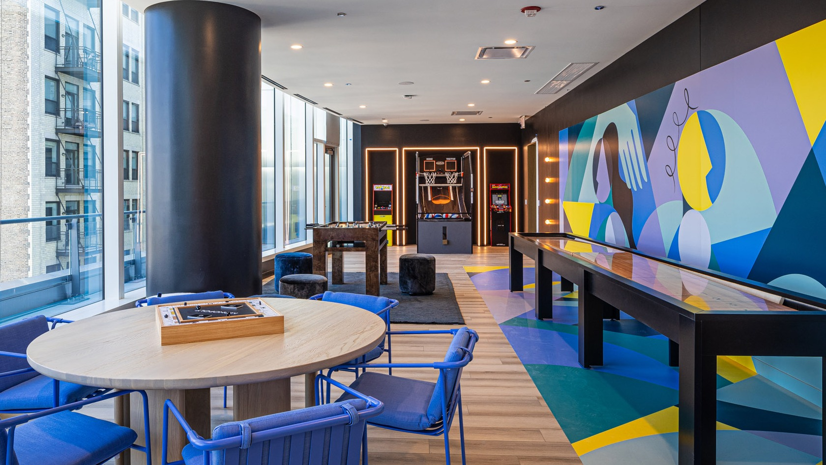 Colorful game room with shuffleboard, arcade basketball, foosball, and casual lounge seating at 1000M Apartments in Chicago