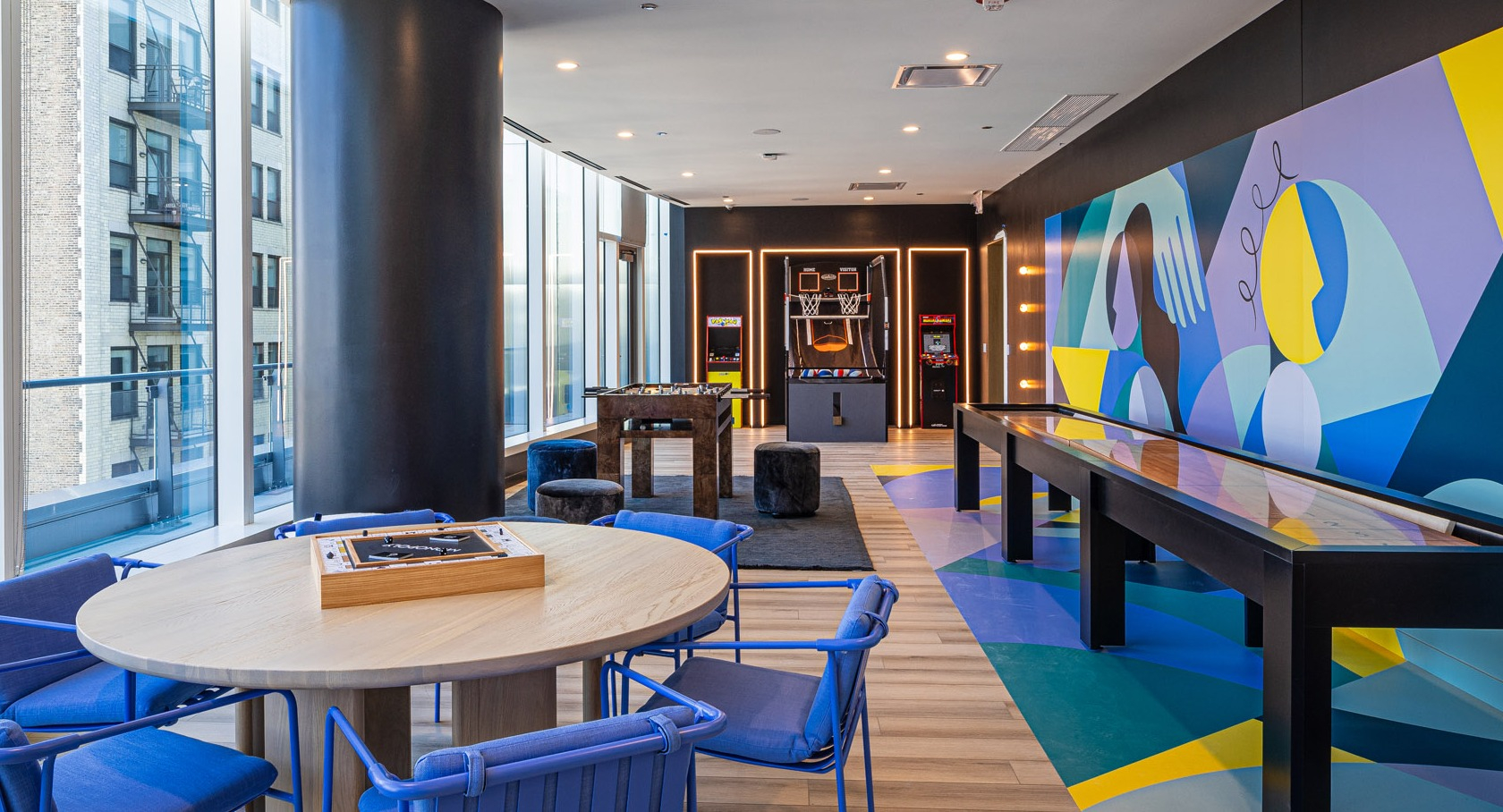 Colorful game room with shuffleboard, arcade basketball, foosball, and casual lounge seating at 1000M Apartments in Chicago