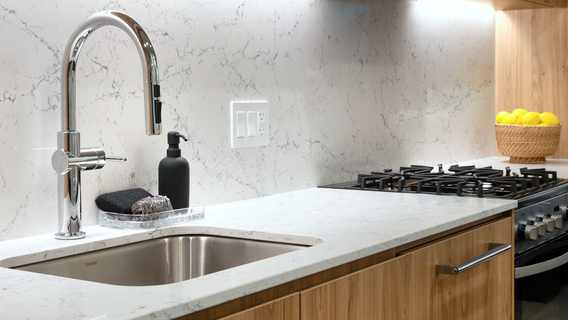 Sleek modern kitchen with marble backsplash, wood cabinetry, stainless steel sink, and gas stove at 1000M Apartments in Chicago