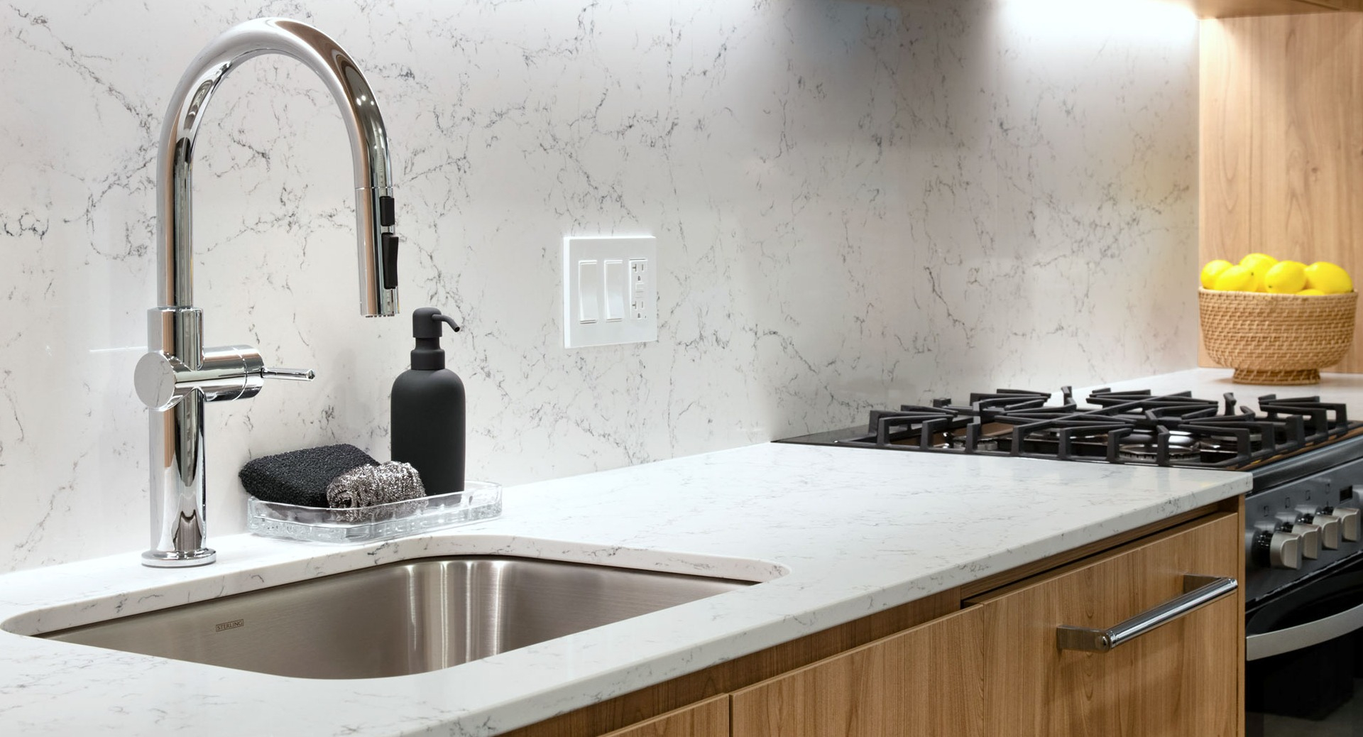 Sleek modern kitchen with marble backsplash, wood cabinetry, stainless steel sink, and gas stove at 1000M Apartments in Chicago