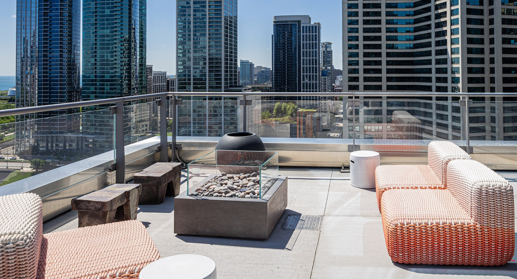Outdoor terrace with woven seating, fire pit, and panoramic views of downtown Chicago skyscrapers at 1000M Apartments