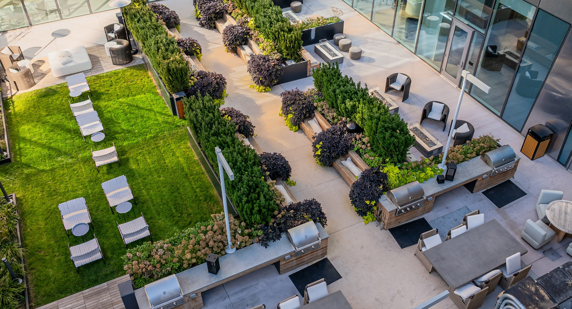 Elevated outdoor social garden featuring grilling stations, fire tables, landscaped seating zones, and lawn loungers at 1000M Apartments in Chicago