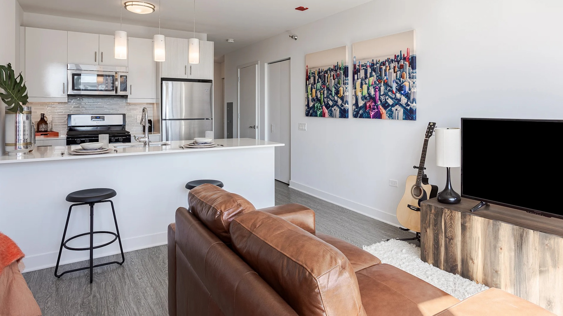 Bright living space at 1001 South State with a leather sofa, TV console, guitar, and wall art next to a modern open kitchen in Chicago