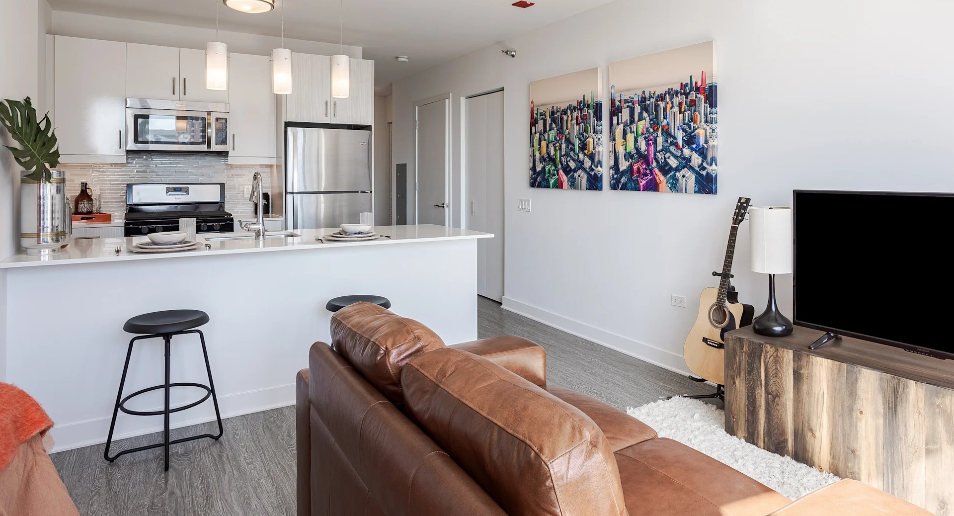 Bright living space at 1001 South State with a leather sofa, TV console, guitar, and wall art next to a modern open kitchen in Chicago