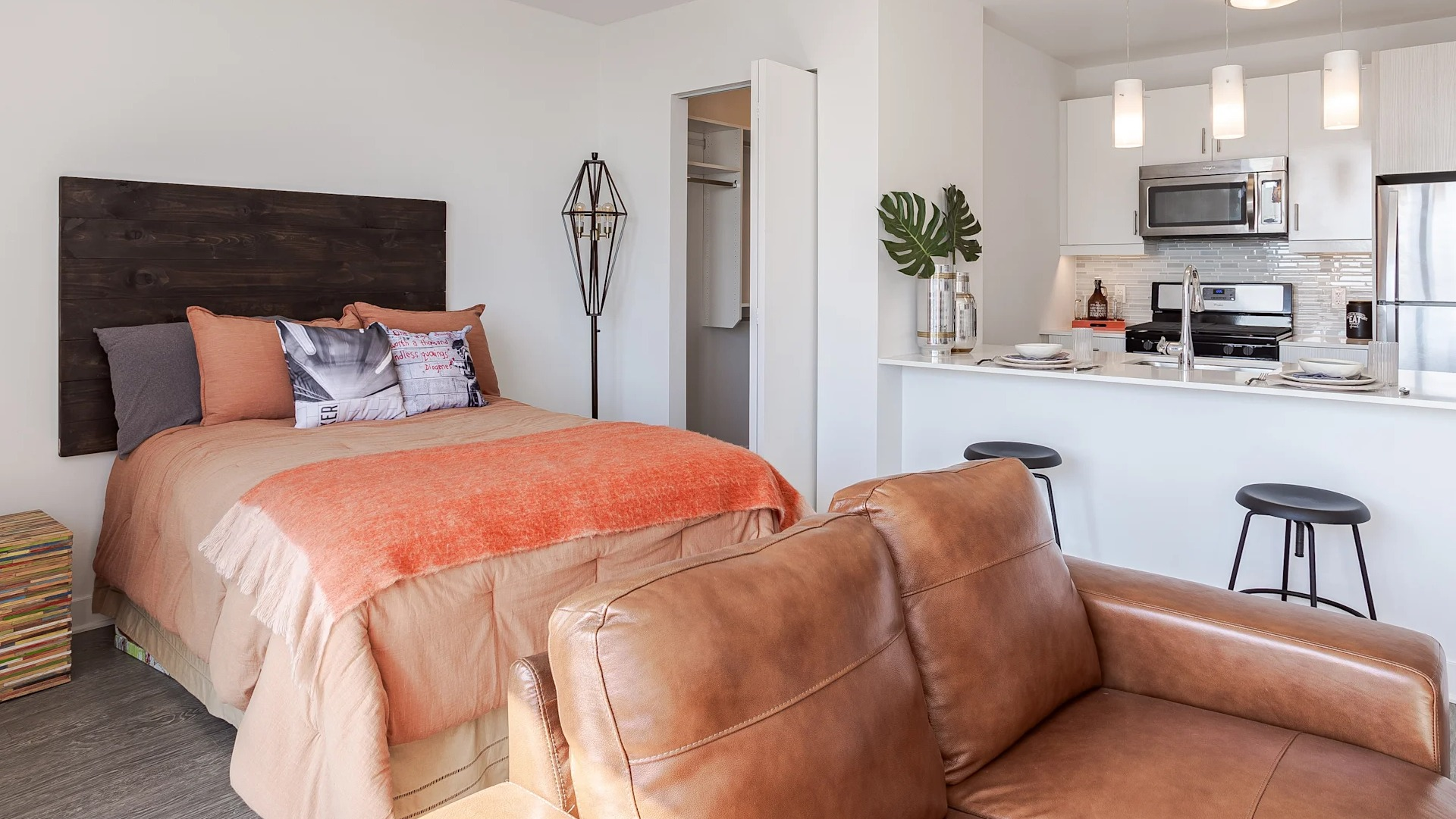 Cozy studio at 1001 South State with a bed, leather sofa, and open kitchen featuring stainless steel appliances and breakfast bar seating