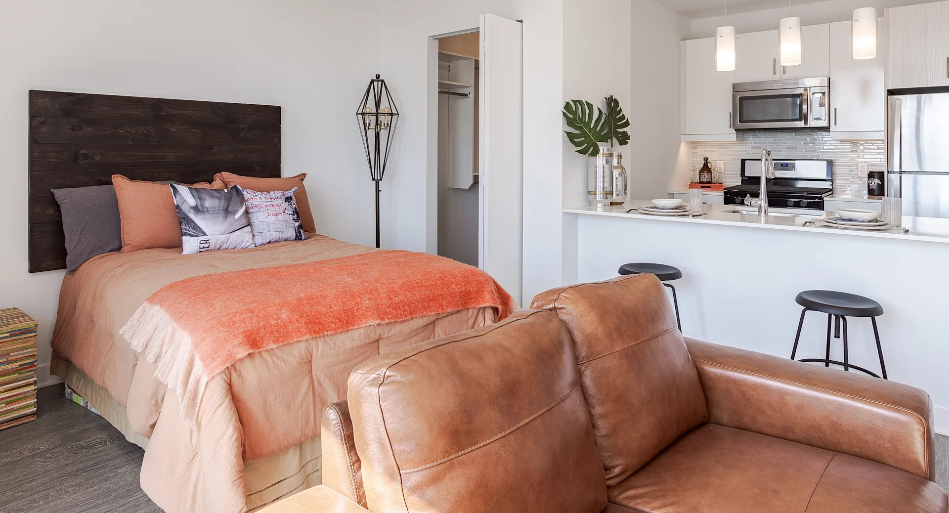 Cozy studio at 1001 South State with a bed, leather sofa, and open kitchen featuring stainless steel appliances and breakfast bar seating