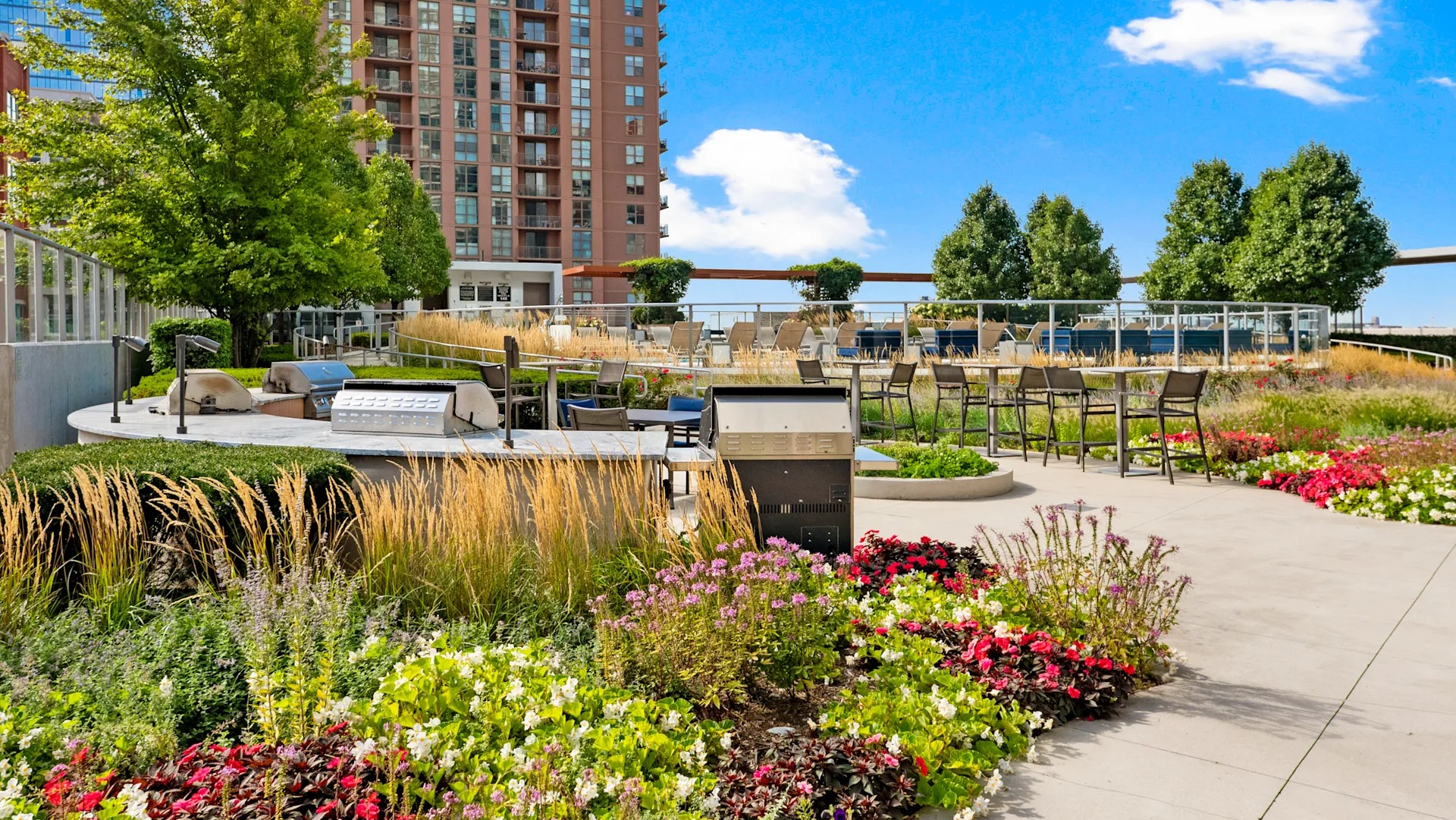 Landscaped terrace with outdoor grills, colorful flowers, and seating areas at 1001 South State apartments in Chicago