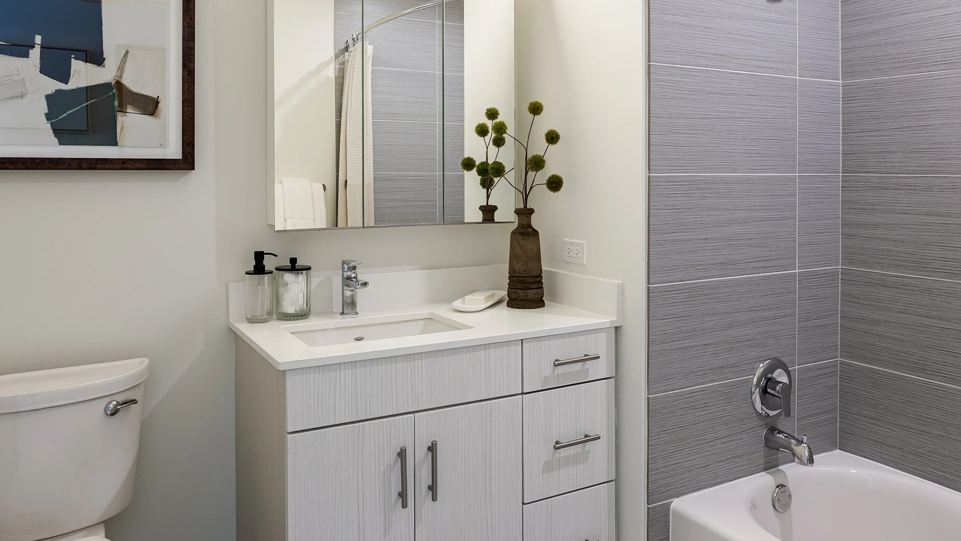 Modern bathroom at 1001 South State featuring gray tiled shower, white vanity with storage, wall mirror, and decorative accents in Chicago
