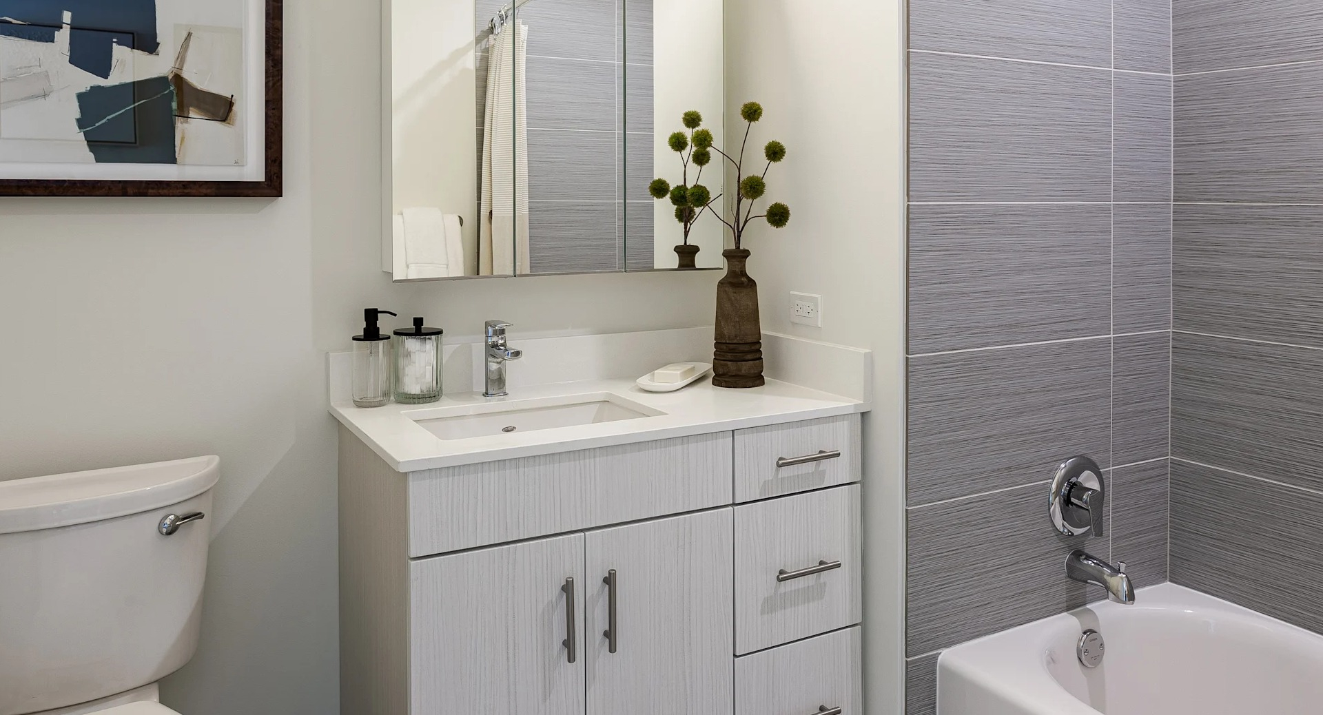 Modern bathroom at 1001 South State featuring gray tiled shower, white vanity with storage, wall mirror, and decorative accents in Chicago