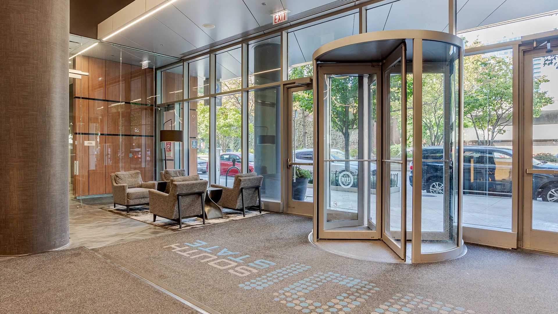 Bright lobby at 1001 South State with a revolving door, glass walls, lounge seating, and tree-lined street views in downtown Chicago