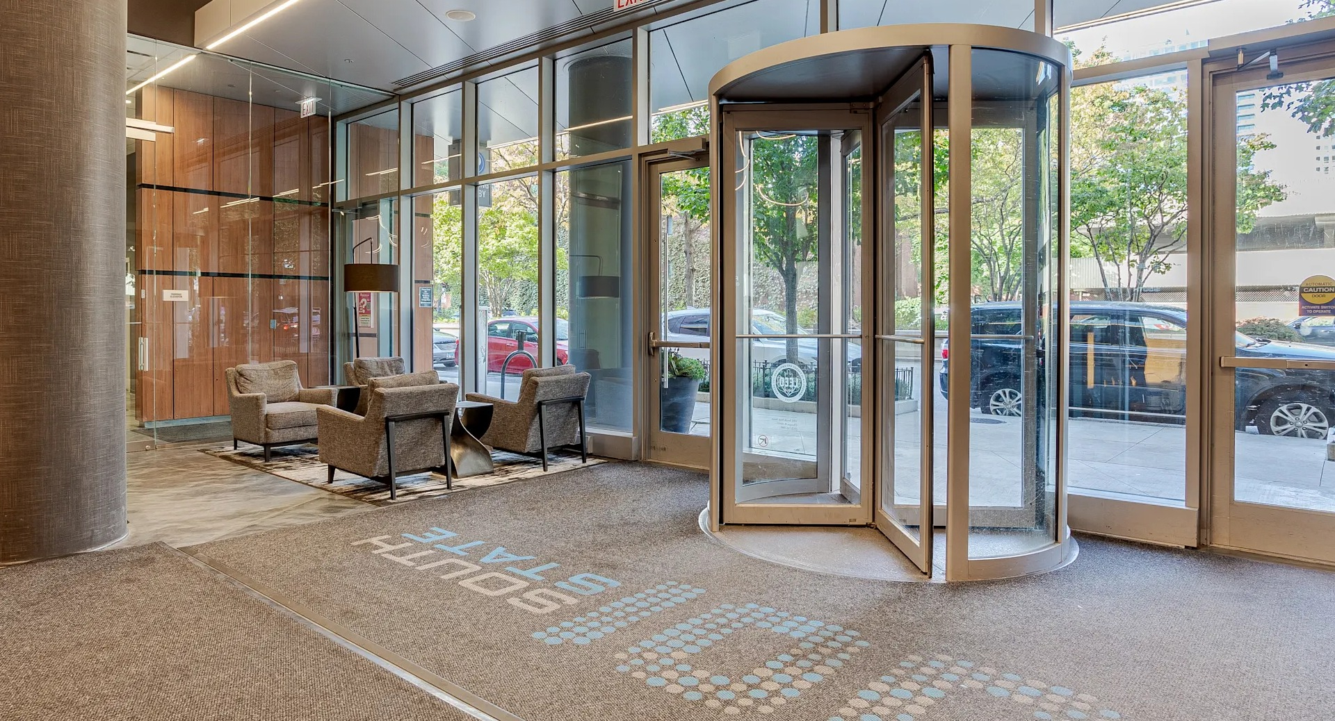 Bright lobby at 1001 South State with a revolving door, glass walls, lounge seating, and tree-lined street views in downtown Chicago