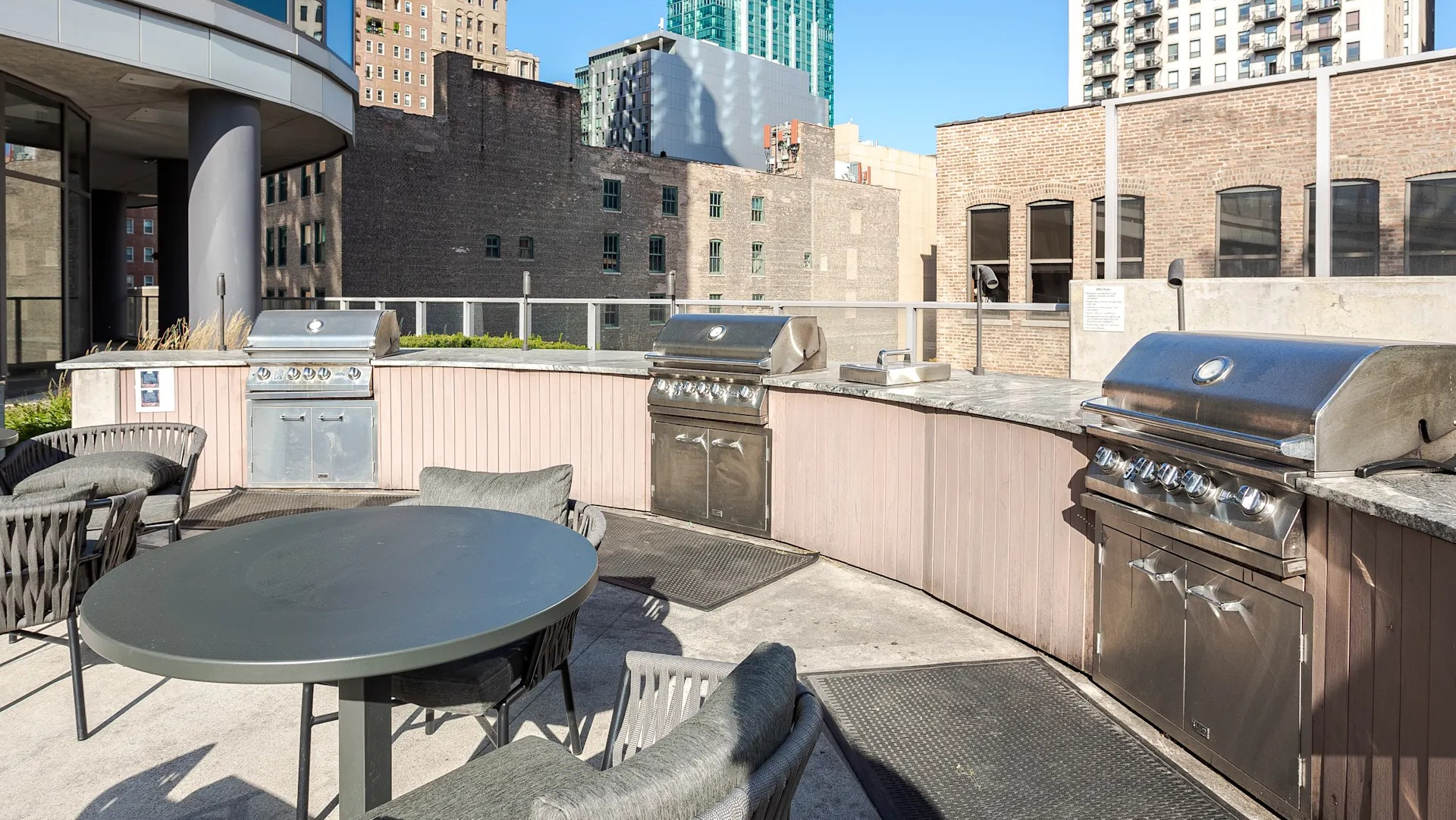 Outdoor grilling stations with stainless steel BBQs, dining tables, and city views at 1001 South State apartments in Chicago