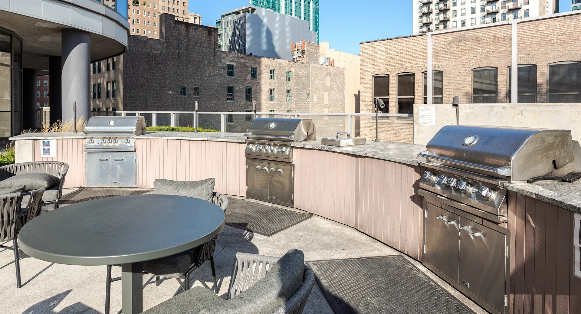 Outdoor grilling stations with stainless steel BBQs, dining tables, and city views at 1001 South State apartments in Chicago