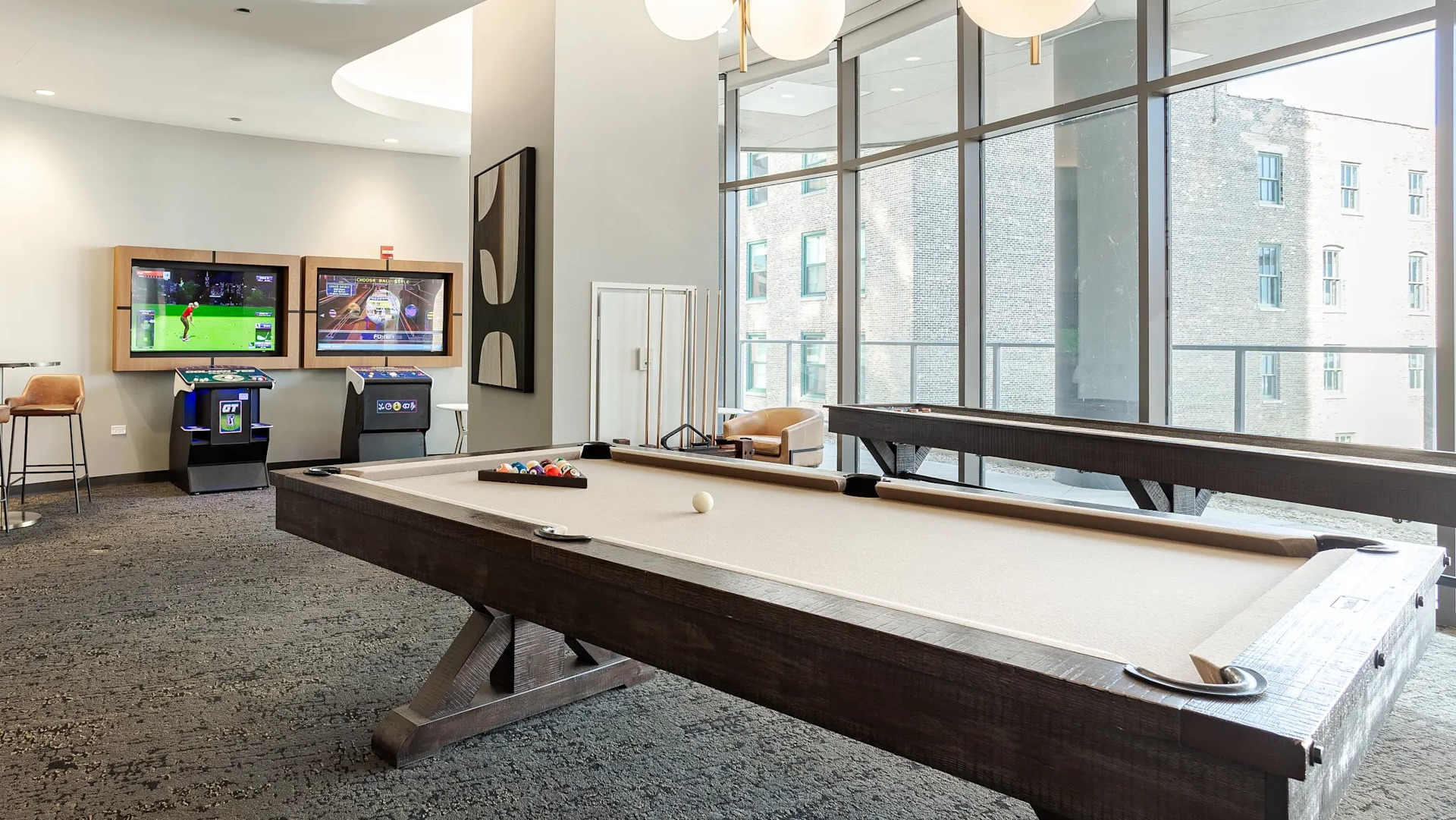 Resident game room with pool table, lounge seating, and entertainment screens at 1001 South State apartments in Chicago