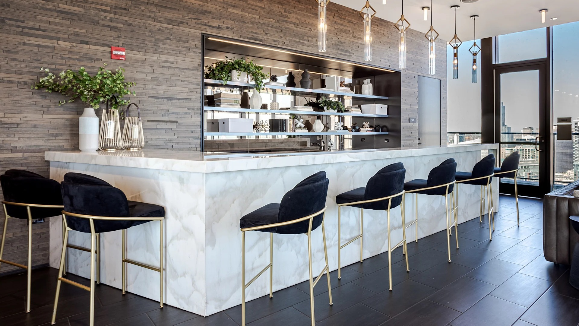 Residents’ bar at 1001 South State showcasing a marble counter, pendant lighting, bar seating, and skyline views from large windows in Chicago