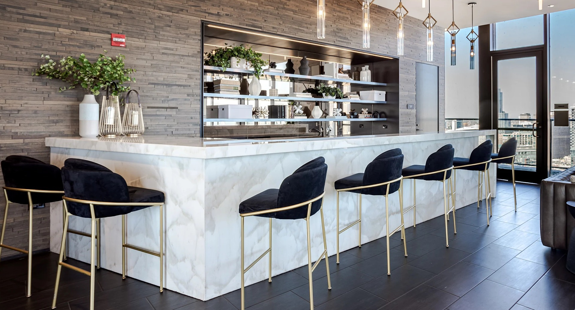 Residents’ bar at 1001 South State showcasing a marble counter, pendant lighting, bar seating, and skyline views from large windows in Chicago