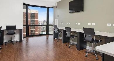Business center with long desk setup, executive chairs, and window views at 1100 North Dearborn apartments in Chicago