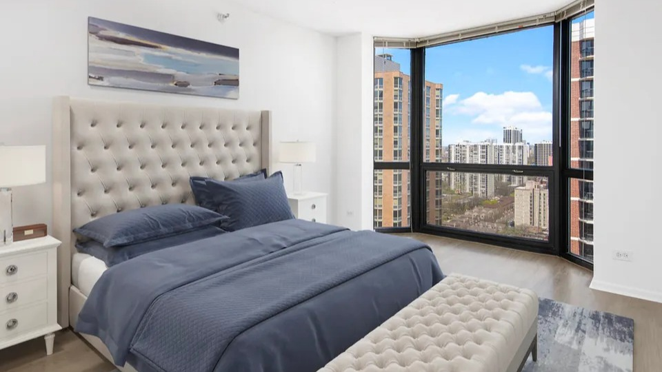 Bright bedroom at 1111 N Dearborn featuring a tufted headboard, bench, and wide city views—elegant finishes in a sought-after Gold Coast Chicago apartment