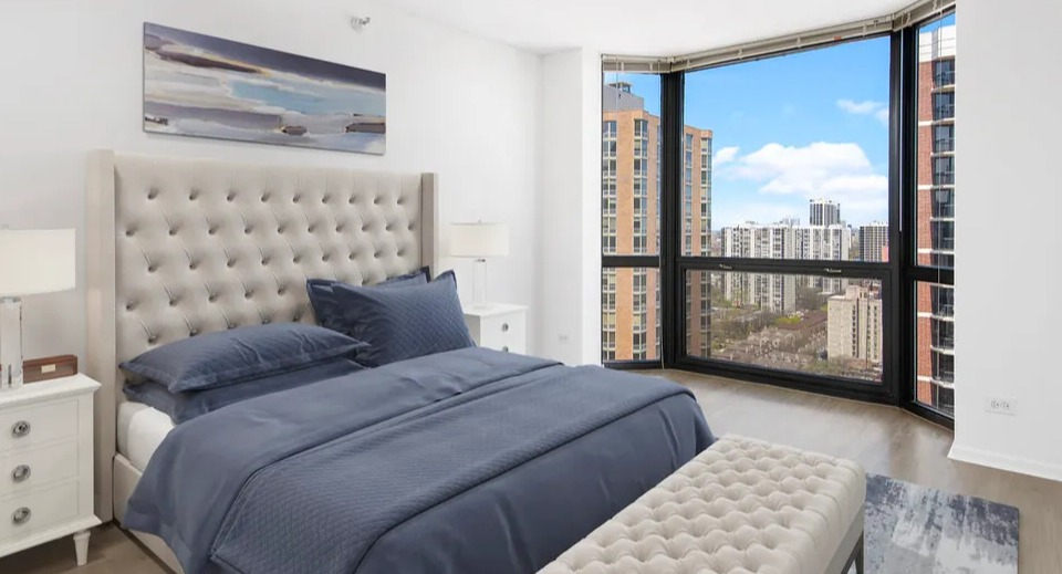 Bright bedroom at 1111 N Dearborn featuring a tufted headboard, bench, and wide city views—elegant finishes in a sought-after Gold Coast Chicago apartment