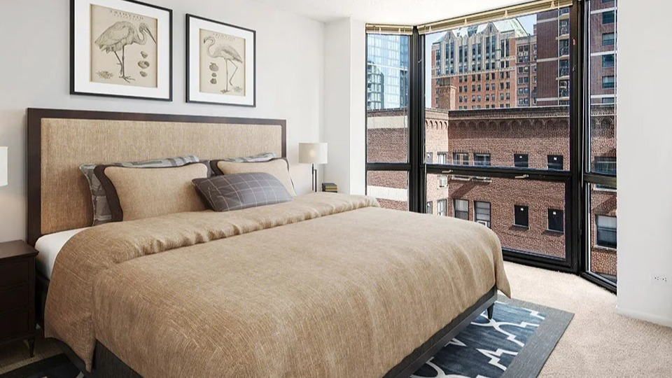 Cozy bedroom at 1111 N Dearborn with a bay window, warm bedding, and city brick views—quiet retreat in a desirable Gold Coast Chicago apartment building