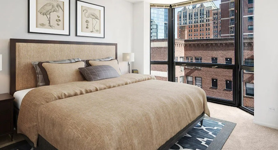 Cozy bedroom at 1111 N Dearborn with a bay window, warm bedding, and city brick views—quiet retreat in a desirable Gold Coast Chicago apartment building