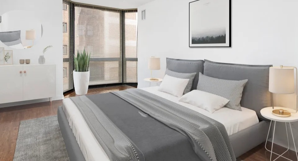 Minimalist bedroom at 1111 N Dearborn with wood floors, sleek gray bedding, and expansive windows with blinds—clean, modern style in a Chicago apartment