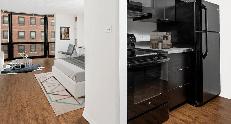 Open studio layout at 1111 N Dearborn showcasing a modern kitchen beside a bright sleeping and living area with large windows—smart use of space in Chicago