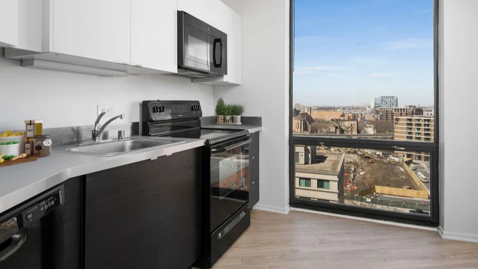Modern galley kitchen with black appliances, microwave, and a large picture window overlooking the city at 1120 N LaSalle in Chicago