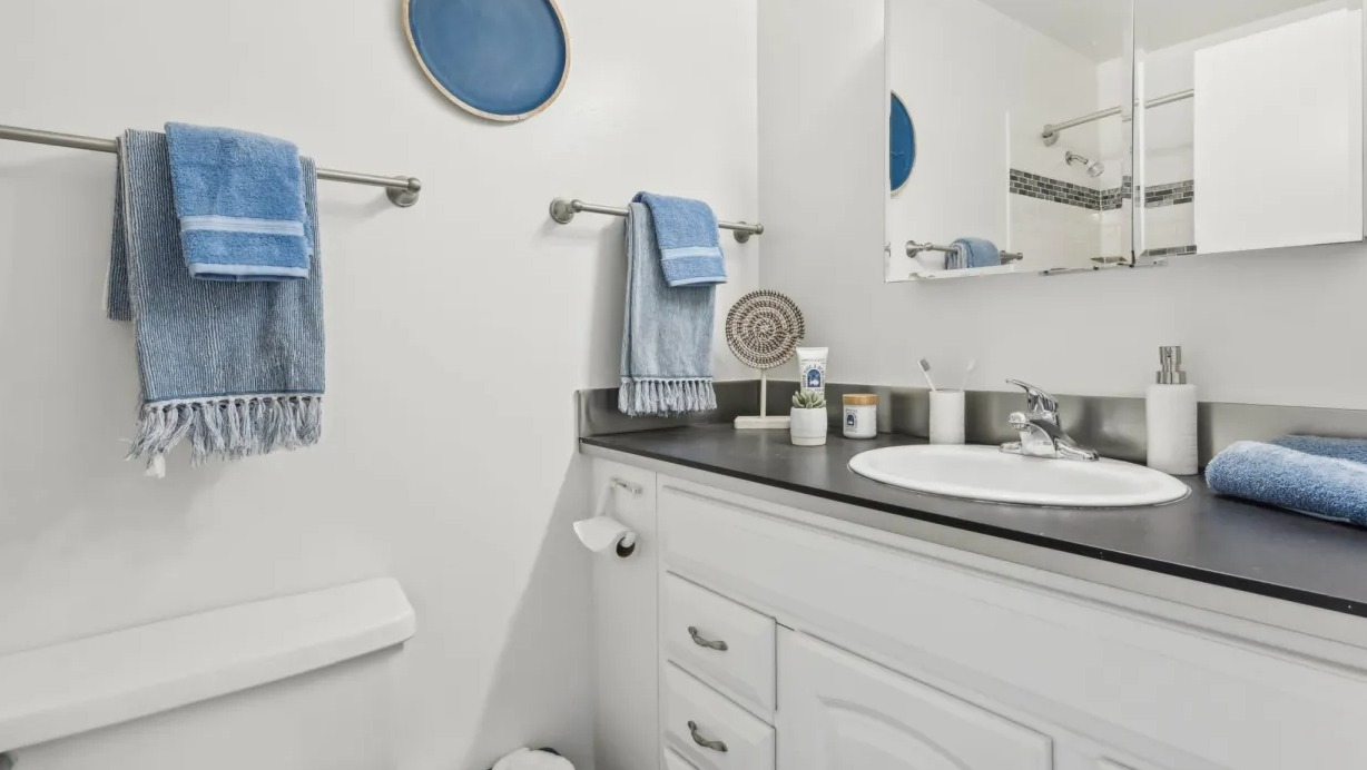 Fresh, clean bathroom with white vanity, large mirror, dark countertop, and blue towel accents at 1133 N Dearborn apartments in Chicago
