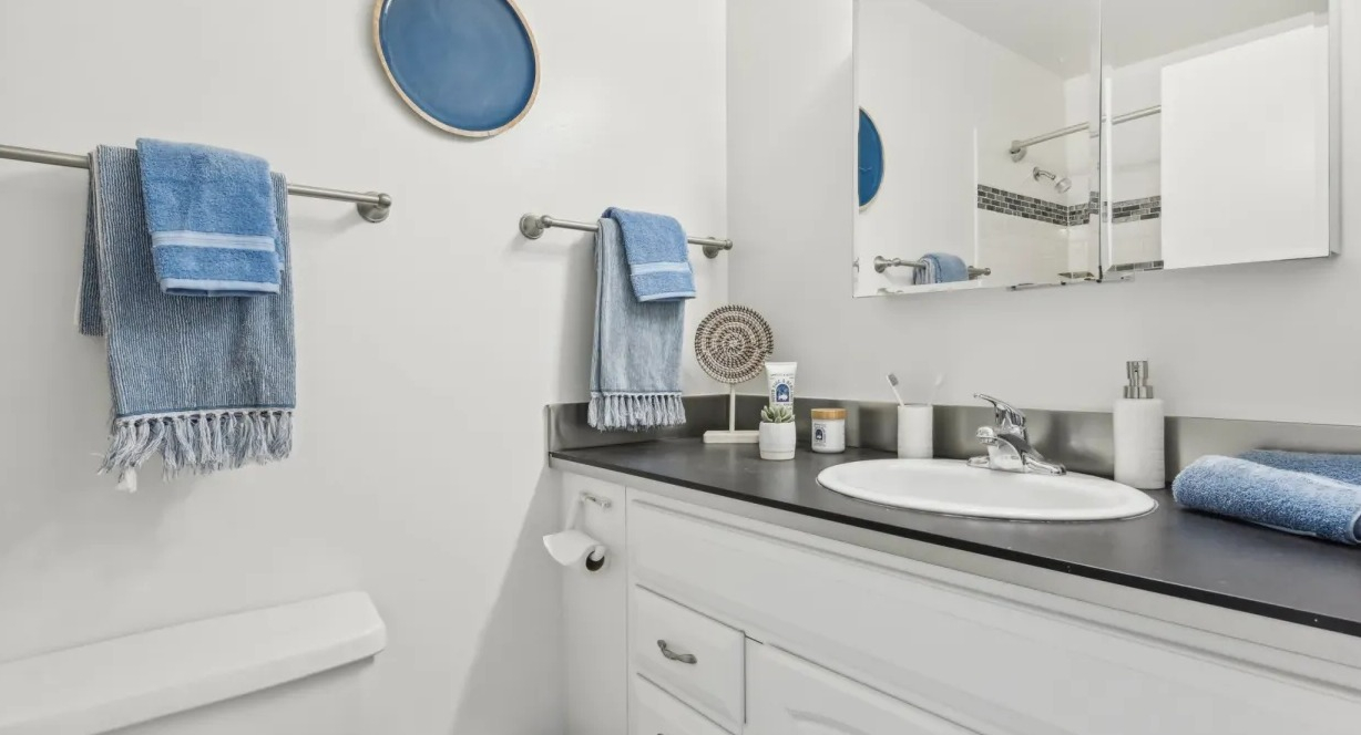 Fresh, clean bathroom with white vanity, large mirror, dark countertop, and blue towel accents at 1133 N Dearborn apartments in Chicago
